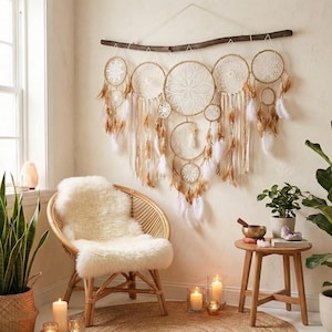 May include: A decorative dreamcatcher, featuring multiple circular frames with white and brown feathers, hangs above a wicker chair with a fluffy white cushion. The room is decorated with candles, plants, and a small wooden table.