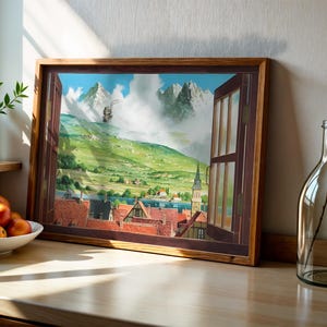 May include: A framed artwork depicts a scenic landscape viewed through an open window. The artwork showcases a village with red-tiled roofs, a church steeple, and mountains in the background. A glass bottle with a handle and a small plant are on the wooden surface.