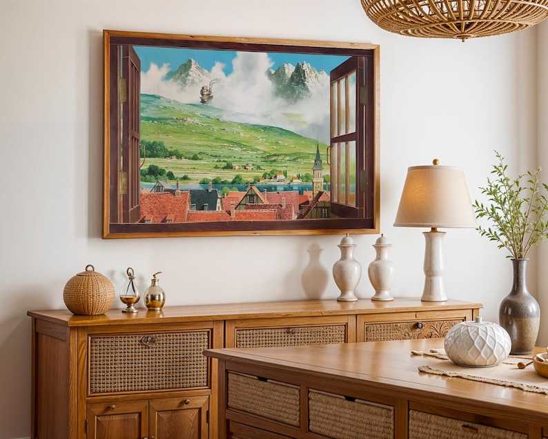 May include: A framed landscape painting depicts a view through an open window. The painting shows a green hillside, a town with red-tiled roofs, and mountains in the distance. A wooden cabinet and table are in the foreground, with decorative items.