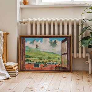 May include: A framed landscape painting depicts a view through an open window. The artwork showcases a green valley, a town with red-tiled roofs, and distant mountains under a cloudy sky. The frame is brown, and the painting is displayed indoors.