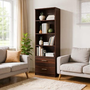 May include: A dark brown wooden bookcase with multiple shelves and two drawers. The shelves display books, decorative vases, and small potted plants. The bookcase is in a living room setting with a window, curtains, and two gray sofas.