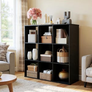 May include: A black cube storage unit filled with decorative items. The shelves display a variety of objects, including vases, boxes, a hat, and a basket. A vase of pink flowers sits on top, adding a pop of color to the room.