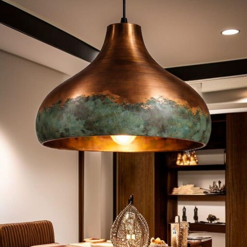 May include: A copper-colored pendant light fixture with a wide, rounded shade. The lower portion of the shade has a band of green patina. The light fixture hangs from a black cord and illuminates the space below.