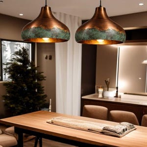 May include: Two copper-colored pendant lights with a green band around the middle hang above a wooden table. The lights have a teardrop shape and are illuminated from within, casting a warm glow.
