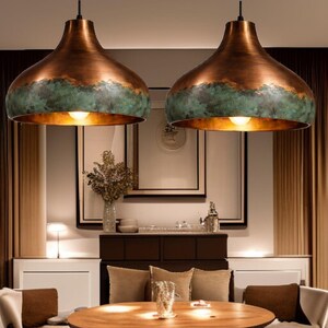 May include: Two copper-colored pendant lights with a verdigris band around the bottom edge. The lights have a bell shape and hang from black cords. The lights are illuminated, casting a warm glow.