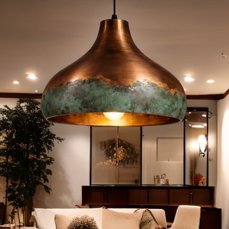 May include: A large, copper-colored pendant light fixture with a unique, inverted bell shape. The fixture has a distressed, verdigris green band around the middle, adding a touch of contrast. The interior is a warm gold color, and the light is on.