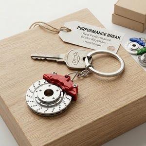 Peut inclure: Un porte-clés avec une clé argentée ornée d'une voiture, un étrier de frein rouge et un rotor de frein argenté. Le porte-clés est attaché à un porte-clés en métal. Une étiquette indique "Performance Break - Red Performance Brake Keychain - Handmade - Etsy."