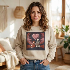 Peut inclure: Sweat-shirt beige avec un motif graphique représentant un squelette, un chien et un cœur rose. Le motif est placé sur un fond sombre avec des accents rouges et roses. Le sweat-shirt est porté par une personne.