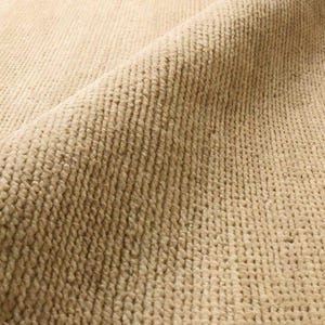 May include: Close-up of a beige woven rug. The rug has a textured surface with a repeating pattern of small, raised loops. The color is a warm, neutral tone, suitable for various interior design styles.