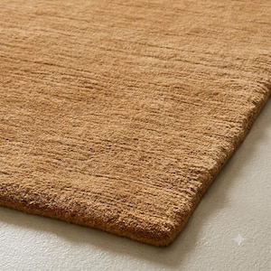 May include: A rectangular area rug in a solid tan color with a dense, short-pile texture. The surface features a consistent, slightly ribbed horizontal weave pattern that creates a uniform appearance across the entire visible fabric surface.
