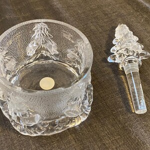 May include: A clear glass jar with a matching tree-shaped bottle stopper. The jar has a textured surface and is decorated with embossed Christmas tree designs. The stopper is also clear and shaped like a Christmas tree.