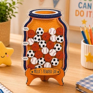 Könnte beinhalten: Ein durchsichtiges Belohnungsglas aus Acryl in Form eines Einmachglases mit gelbem Punktemuster. Es enthält kleine Holzplättchen in Form von Fußbällen, Baseballs und Basketbällen. Der Sockel ist mit "Mila's Reward Jar" beschriftet.