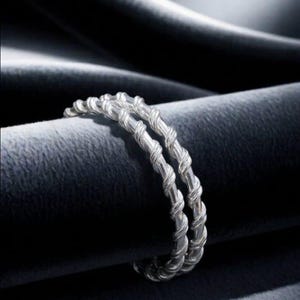 May include: A double-band ring featuring a twisted rope-like texture crafted from a bright, reflective silver-toned metal. The two bands are joined together, creating a continuous, uniform spiral pattern that wraps around the entire circumference.
