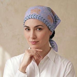 May include: A light purple bandana featuring a repeating pattern of orange butterfly-like shapes and a green leaf-patterned border. The fabric is tied at the back of the head, displaying a soft, lightweight texture with a distinct botanical motif.