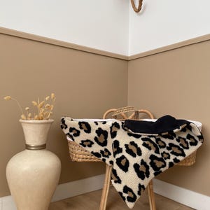 Peut inclure: Un berceau pour bébé en osier avec une couverture à imprimé léopard et une couverture noire. Le berceau est sur un cadre en bois. Une tête d'éléphant décorative est accrochée au mur au-dessus du berceau.