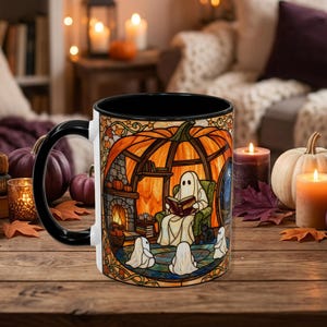 May include: A white ceramic mug with a black handle and interior, featuring a colorful stained-glass style illustration of a ghost reading a book in a pumpkin-shaped room, surrounded by smaller ghosts and a black cat near a fireplace.