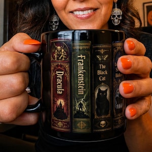 May include: A black ceramic mug featuring a graphic print of vintage book spines with titles including Dracula, Frankenstein, and The Black Cat. The design includes detailed illustrations of a gargoyle, a lightning storm, and a black cat, all set against a dark, gothic-inspired background.