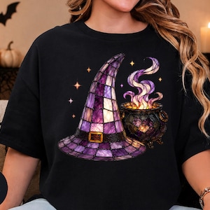 Könnte beinhalten: Ein schwarzes T-Shirt mit einem Grafikdruck eines violetten Hexenhuts im Buntglas-Stil und einem passenden Kessel mit wirbelndem violett-weißem Rauch, akzentuiert durch kleine gelbe Sterne auf dem dunklen Stoffhintergrund.