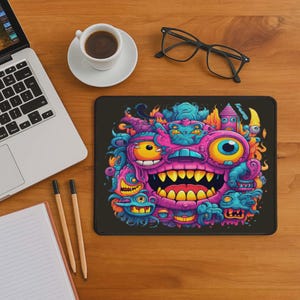 May include: A black rectangular mousepad featuring a colorful cartoon monster design with a large mouth, multiple eyes, and various other creature-like elements. The design incorporates pink, yellow, blue, and orange hues.