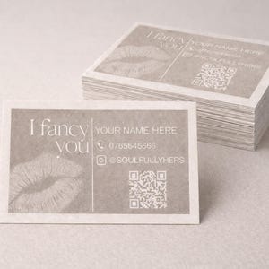 May include: A pile of business cards with a light grey hue. The cards display the text "I fancy you" and "YOUR NAME HERE", a lip print, a phone number, and a social media handle. A QR code is also visible.