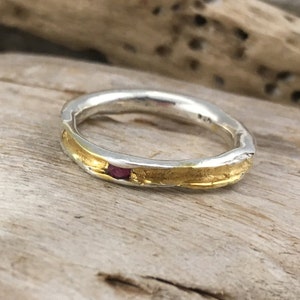 Könnte beinhalten: Ein silberner Ring mit einem dünnen Goldband und einem kleinen rosafarbenen Edelstein.