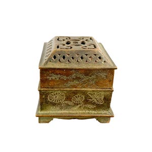 May include: A rectangular bronze-toned metal incense burner featuring a removable lid with an intricate openwork geometric pattern. The base and lid sides are decorated with engraved floral motifs, including chrysanthemums and a butterfly.