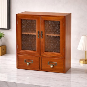May include: A wooden cabinet with a warm brown finish. It features two glass doors with a textured pattern and two drawers with metal handles. The cabinet is designed for storage and display.
