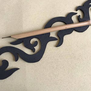 Peut inclure: Un stylo de calligraphie en bois avec une plume noire reposant sur un motif décoratif noir. Le motif est fait d'un matériau noir épais et a une forme organique et fluide.