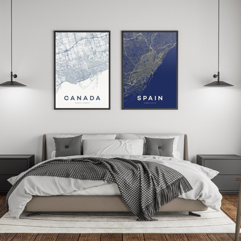 Pode incluir: Duas impress&otilde;es emolduradas de mapas, uma com a etiqueta "CANADA" e a outra "SPAIN", est&atilde;o penduradas acima de uma cama. O mapa do Canad&aacute; &eacute; azul claro e branco, enquanto o mapa da Espanha &eacute; azul marinho e dourado. A cama tem um cobertor e almofadas cinzentas.