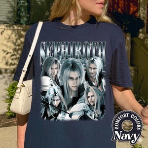 Puede incluir: Camiseta azul marino con un gráfico del personaje Sephiroth. El diseño muestra múltiples imágenes del personaje con largo cabello plateado. La palabra "SEPHIROTH" está impresa en la parte superior en una fuente plateada y metálica. La camiseta también tiene las palabras "COMFORT COLORS" y "Navy".