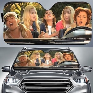 Peut inclure: Pare-soleil de voiture avec un groupe de femmes dans une voiture, avec des expressions surprises et excitées. L'image est imprimée sur un pare-soleil noir, conçu pour s'adapter à un pare-brise de voiture. Le pare-soleil est montré installé dans une voiture grise.
