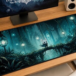 May include: A rectangular desk mat featuring a dark, teal-toned forest scene with glowing lanterns hanging from vines. A small, white, horned character with a dark cloak stands on a bridge in the center of the lush, shadowed woodland environment.