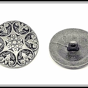 Puede incluir: Un botón de metal plateado con un diseño floral decorativo. La parte posterior del botón es lisa.