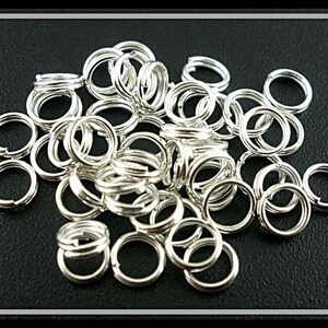 May include: A large pile of silver jump rings, a type of jewelry finding, on a black background.