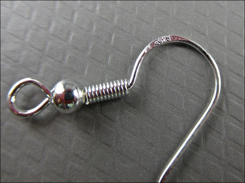 May include: Silver earring hook with a spring coil and a ball at the top. The hook is marked with "925" indicating it is made of sterling silver.