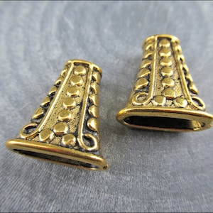 Puede incluir: Dos tapones de metal dorado con un diseño decorativo. Los tapones tienen una superficie texturizada con un patrón en relieve de círculos y líneas.