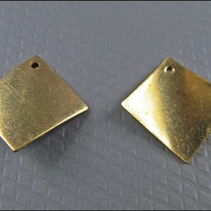 Puede incluir: Dos dijes de metal en forma de diamante de color latón. Cada dije tiene un pequeño agujero en la parte superior para colgar. Los dijes tienen una apariencia ligeramente desgastada, lo que sugiere que son vintage o hechos a mano. Ideales para la creación de joyas o proyectos de artesanía.