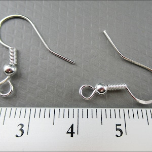 May include: Two silver earring hooks with spring-loaded closures. The hooks are measured against a ruler, showing they are approximately 1.5 inches long.