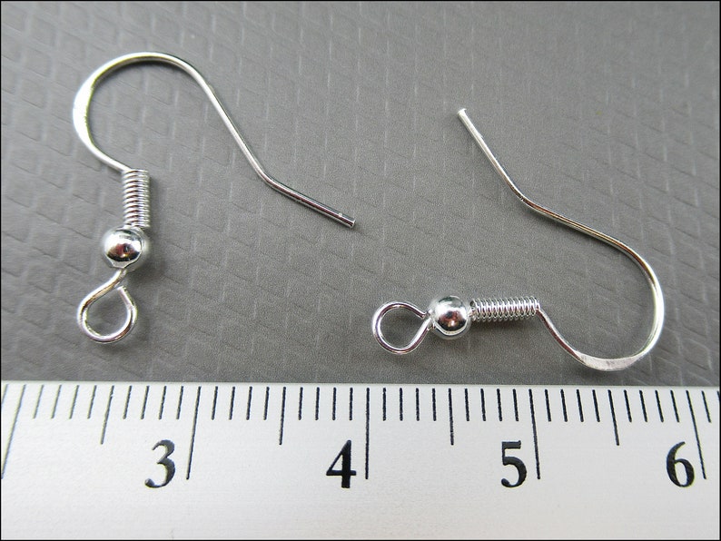 May include: Two silver earring hooks with spring-loaded closures. The hooks are measured against a ruler, showing they are approximately 1.5 inches long.