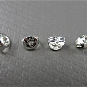 Può includere: Quattro dorsi di orecchini in argento, ognuno con un design diverso. I dorsi sono contrassegnati dal numero "925", a indicare che sono in argento sterling.