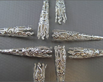 May include: Silver metal cone-shaped bead caps with intricate designs. The caps are approximately 2.5 cm long and have a pointed tip.