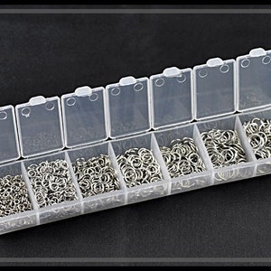 Puede incluir: Una caja de almacenamiento de plástico transparente con 10 compartimentos llenos de anillos de salto plateados. La caja está abierta y los anillos de salto son visibles.