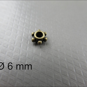 May include: A bronze-colored metal bead with a 6 mm diameter. The bead has a starburst design with six points.