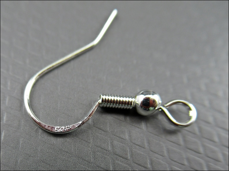May include: Silver earring hook with a ball at the end and a spring-loaded closure. The hook is marked with "925" indicating it is made of sterling silver.