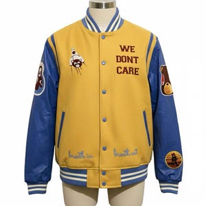 以下が含まれることがあります： 前面に「WE DON'T CARE」の文字が入った、黄色と青色のスタジアムジャンパー。青い袖と、クマや漫画のキャラクターなど、複数のパッチが付いています。「breath in」と「breath out」の文字が前面に刺繍されています。
