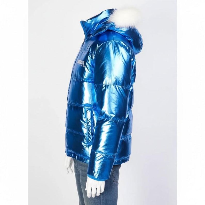 May include: A shiny, metallic blue puffer jacket with a hood trimmed with white faux fur. The jacket has a quilted design and a small logo on the chest. The model is wearing blue jeans.