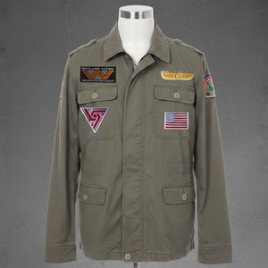 May include: An olive green jacket with various patches, including an American flag and the text "MAYLAND YUTANI". The jacket features four front pockets and a button-down closure. It is displayed on a mannequin.