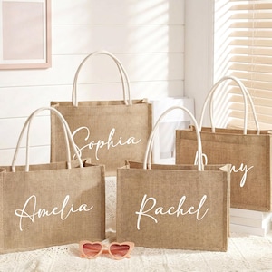 May include: Four personalized burlap tote bags with white handles. Each bag has a different name in elegant white script: Amelia, Sophia, Rachel, and Amy. Pink heart-shaped sunglasses rest in front of the bags.