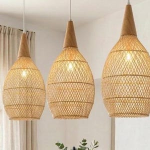 Könnte beinhalten: Drei Hängeleuchten mit geflochtenen, hellbraunen Rattanschirmen und hellen Holzaufsätzen über einem rechteckigen Holzesstisch. Der Tisch ist mit blau-weiß gemusterten Keramiktellern, Schüsseln und blauen Stoffservietten gedeckt.
