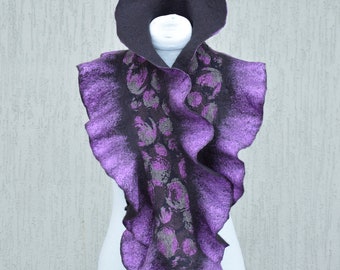 May include: A felted scarf with a hood, displayed on a mannequin. The scarf is primarily purple with a ruffled edge and a floral pattern in gray. The hood is black.